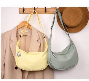 Detail view of crescent crossbody bags in light yellow and green hanging on a wooden rack