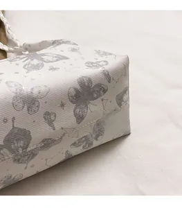 Close-up of white tote bag featuring grey butterfly prints and cross-grain leather texture
