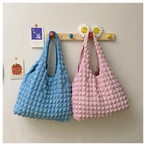 Macro detail of bubble textured fabric on blue and pink waffle tote bags hanging on a rack