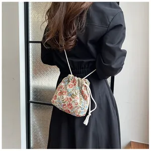 Close-up of a floral drawstring bucket bag with colorful embroidery and cream shoulder strap