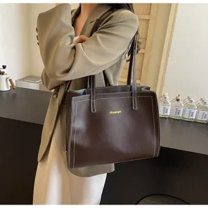 Détail du sac cabas marron foncé avec surpiqûres blanches et logo doré sur cuir mat