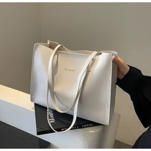 Détail du sac cabas blanc minimaliste avec logo doré sur un magazine blanc épuré