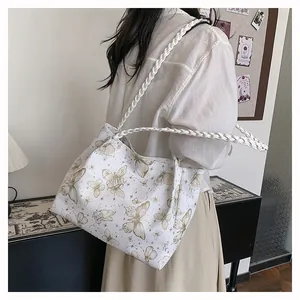 Detail of white tote bag with golden butterfly prints and woven shoulder strap