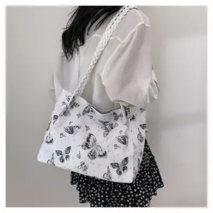 Detail of white tote bag featuring black butterfly prints and woven shoulder strap