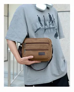 Detail of a brown canvas crossbody bag with triple zippers on a male model's shoulder
