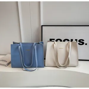 Détail de cabas minimalistes bleu et blanc avec logo doré et surpiqûres apparentes