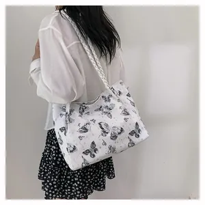 Detailed side view of white tote bag with black butterfly patterns and woven strap