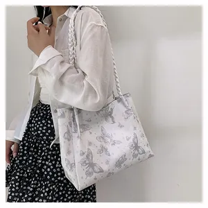 Close-up of white tote bag with purple butterfly prints and woven shoulder strap details
