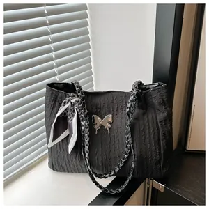 Detail of black tote bag featuring pleated texture, silver butterfly and woven handle