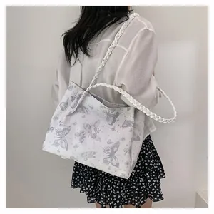 Detail of a white canvas tote bag with butterfly prints and woven shoulder straps