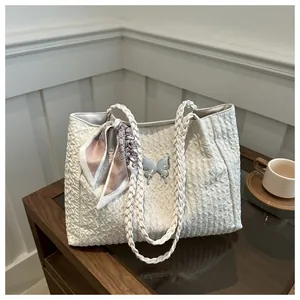 Detail of cream tote bag featuring quilted texture, woven handles, and silver butterfly charm