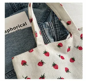Close-up van witte corduroy draagtas met rode aardbeienpatronen en gedetailleerde afwerking