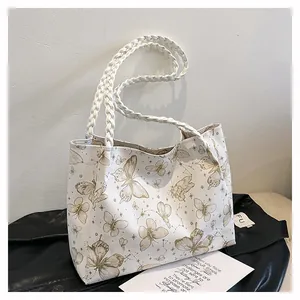 Detail of white tote bag with gold butterfly prints and woven rope handles on black leather
