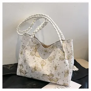 Close-up of white tote bag with golden butterfly print and woven handle detail