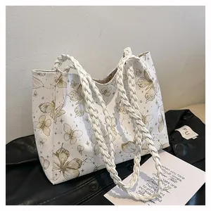 Detail of white tote bag with gold butterfly print and woven handles on leather jacket