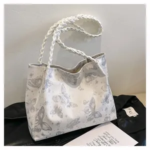 Detail of white butterfly print tote bag with woven handles on textured leather surface