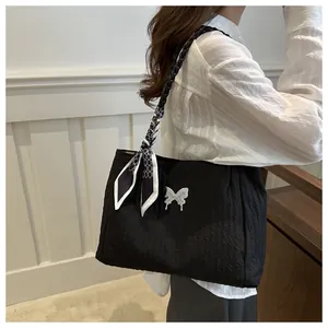 Detail of black textured tote bag featuring woven straps, silk scarf, and silver butterfly