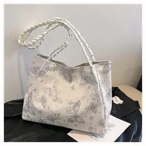 Detail of white tote bag with gray butterfly print and woven handles on leather jacket