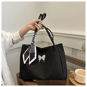 Detail of black pleated tote bag with white bow accent and patterned silk scarf handle