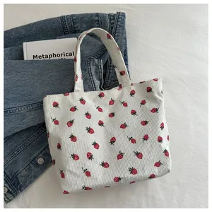 Close-up of white corduroy tote bag featuring vibrant red strawberry patterns on denim