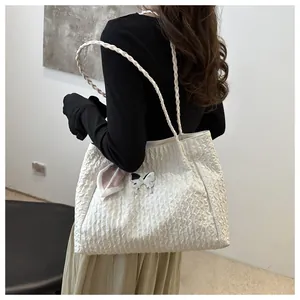 Detail of white pleated tote bag featuring woven straps and metallic butterfly ornament