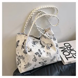 Detail of white tote bag featuring black butterfly print and woven leather straps