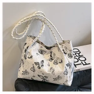 Detail of white tote bag featuring black butterfly prints and woven shoulder straps