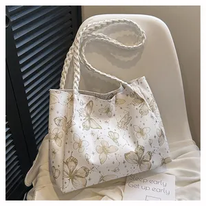 Detailed close-up of white tote bag featuring gold butterfly prints and woven handles