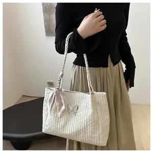 Detail of a beige pleated tote bag featuring a metal butterfly clasp and woven handle