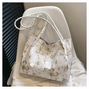 Detail of white leather tote bag with gold butterfly pattern and woven shoulder straps