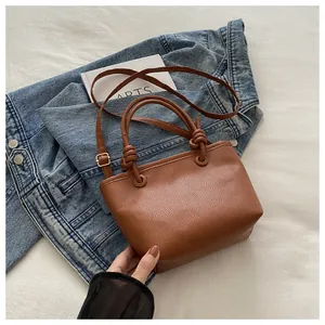 Detail of brown lychee grain leather bucket bag with unique knot handle on denim jacket