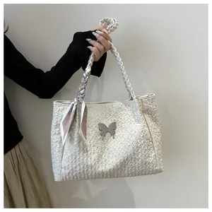 Detail of creamy white pleated tote bag with silver butterfly charm and woven handle