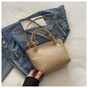 Close-up of beige lychee grain bucket bag with knotted handle on denim jacket background
