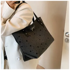 Detail of dark grey tote bag with black star prints and silver bow pendant on model