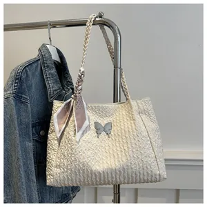Close-up of white pleated tote bag with silver butterfly charm and silk scarf handle