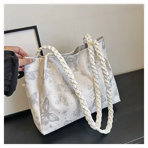 Detail of white tote bag featuring grey butterfly prints and woven handles on a black surface