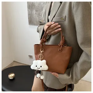 Close-up of brown pebbled leather bucket bag with knotted handle and plush cloud charm