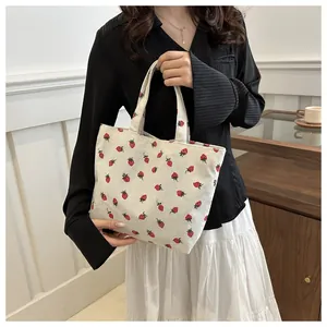 Detail of white corduroy tote bag featuring vibrant red strawberry patterns and sturdy handles