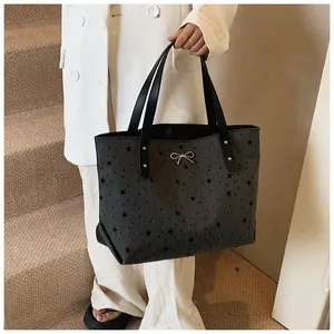 Detail of grey tote bag featuring black stars, metallic bow, and sturdy black handles