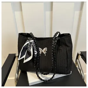 Detail of black pleated tote bag with silver butterfly buckle and woven shoulder strap