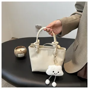 Detail view of cream bucket bag with thick rope handle and cute plush cloud charm