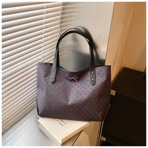 Close-up of grey tote bag with red heart pattern, metal bow buckle and leather handles