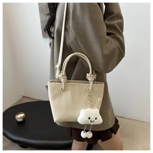 Close-up of cream leather bucket bag with knot handle and plush cloud charm detail