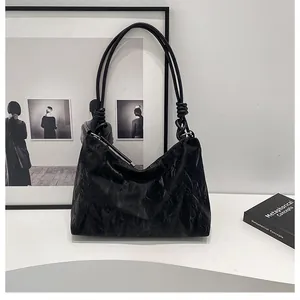 Detail of black pleated leather tote bag featuring slim knotted shoulder straps and zipper