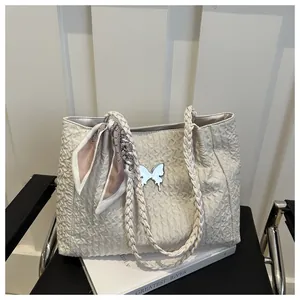 Detail of cream tote bag featuring wavy quilted texture, silver butterfly and woven handle