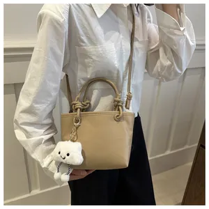 Detail of khaki bucket bag with knot handle and plush cloud charm worn by a model