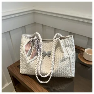 Detail of cream woven tote bag featuring a silver butterfly charm and patterned silk scarf