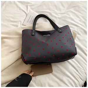 Detailed close-up of a large grey polka dot tote bag with a silver metal bow decoration