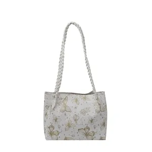 White tote bag featuring golden butterfly prints and woven handles on a plain white background