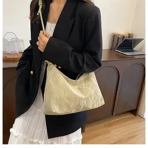 Close-up of pleated beige hobo bag with zipper and shoulder strap on model in black suit
